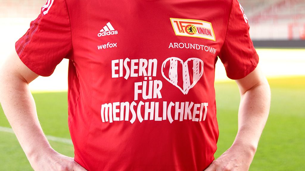 Roter Trikot mit Schriftzug "EISERN FÜR MENSCHLICHKEIT" und Vereinslogo von Union Berlin.