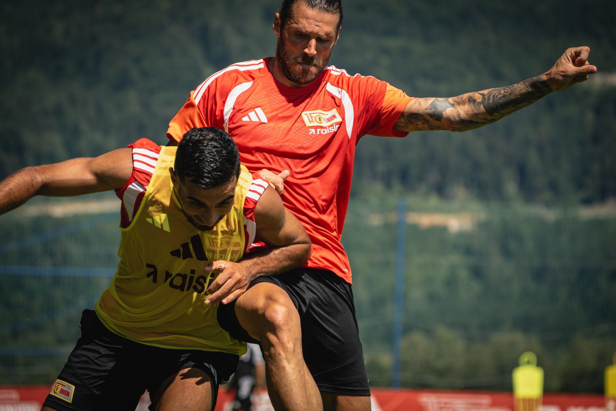 Zwei Fußballspieler in einem Wettbewerbsszenario während eines Trainings, einer in gelber und einer in roter Sportkleidung.