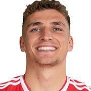 Ein junger Mann mit kurzen, lockigen Haaren, lächelt in einem roten Sporttrikot.