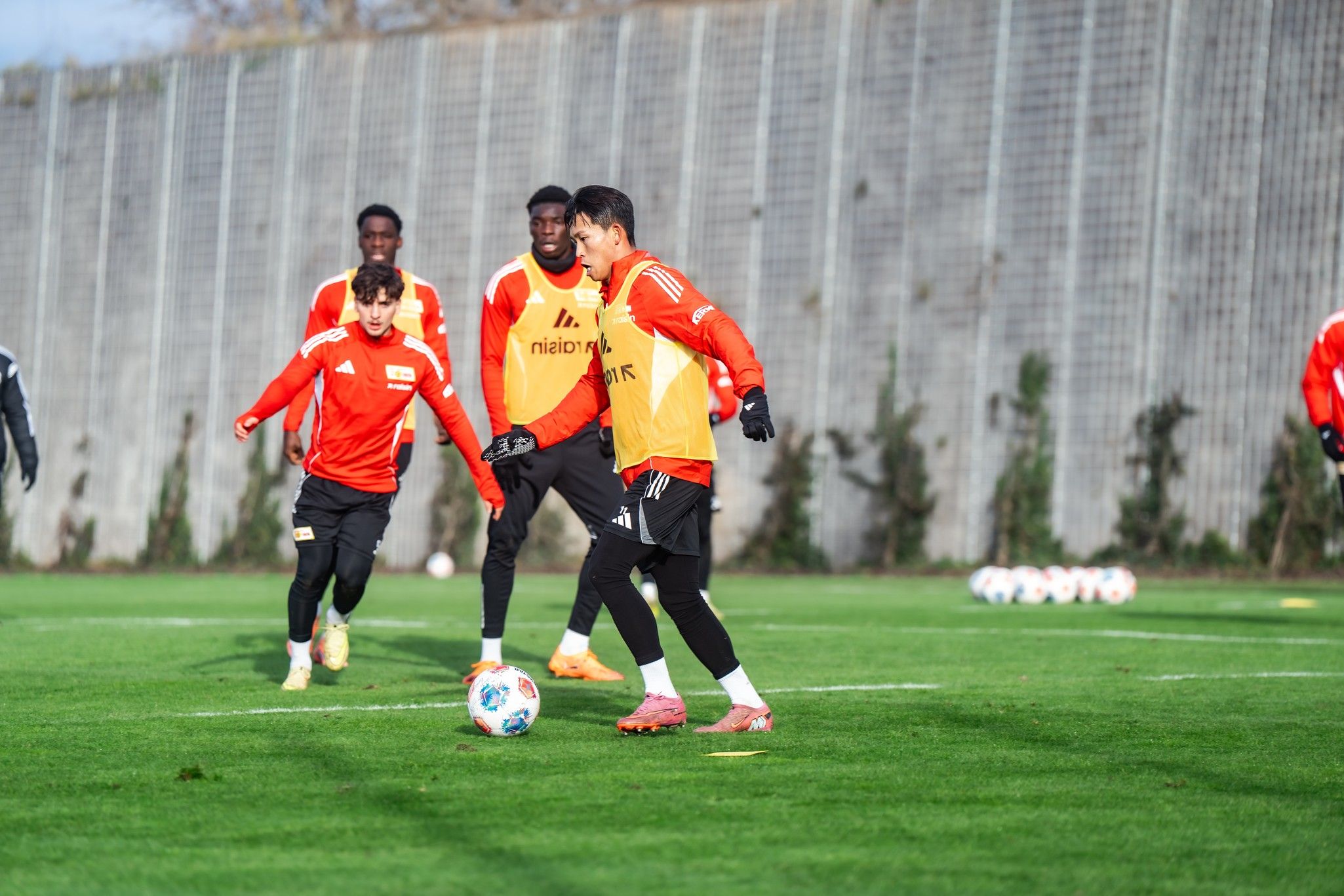 A soccer team is training on a grass field while a player dribbles the ball.