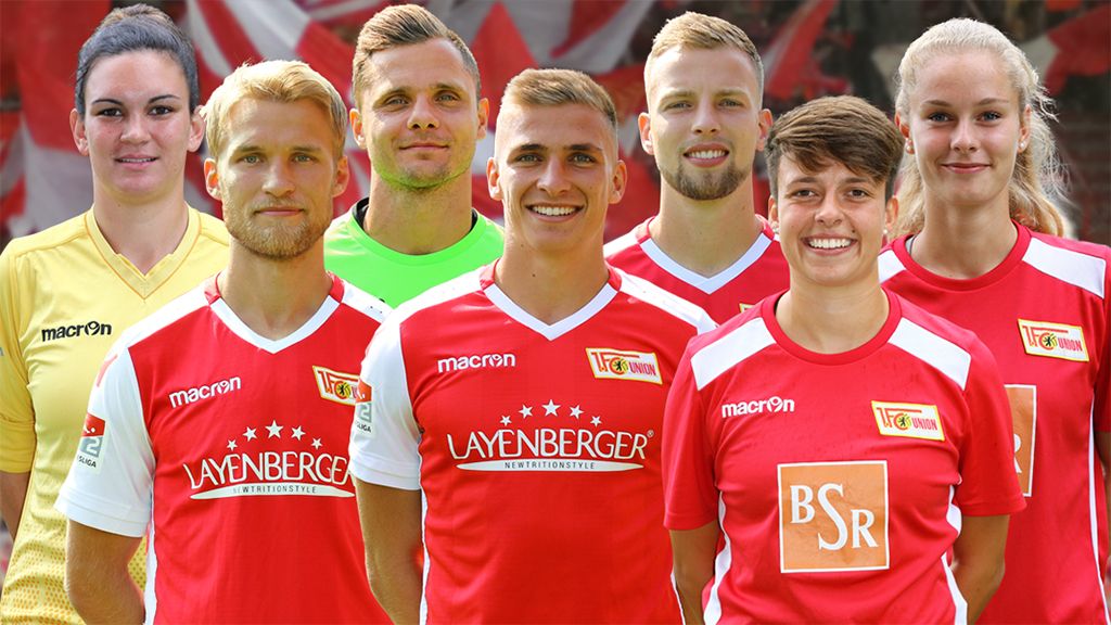 A group of seven athletes in red jerseys with a club logo, posing in front of a blurred background.