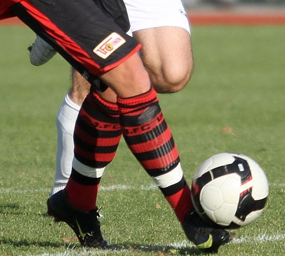 Ein Fußballspieler in gestreiften Socken tritt einen Fußball auf dem Rasen.