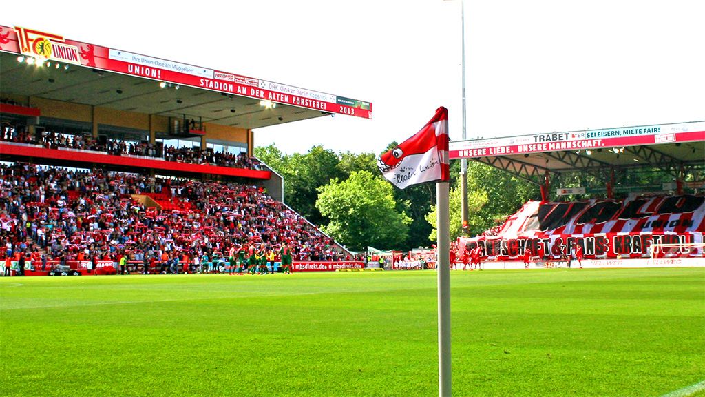 A stadium view with fans supporting a game and a flag in the foreground.