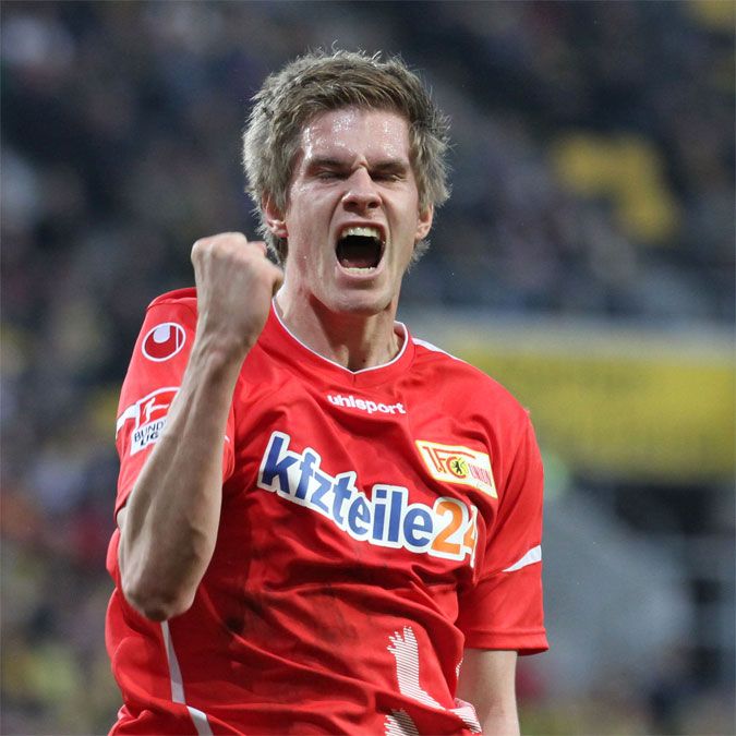 Ein junger Fußballspieler in rotem Trikot jubelt leidenschaftlich und zeigt die Fäuste nach oben.