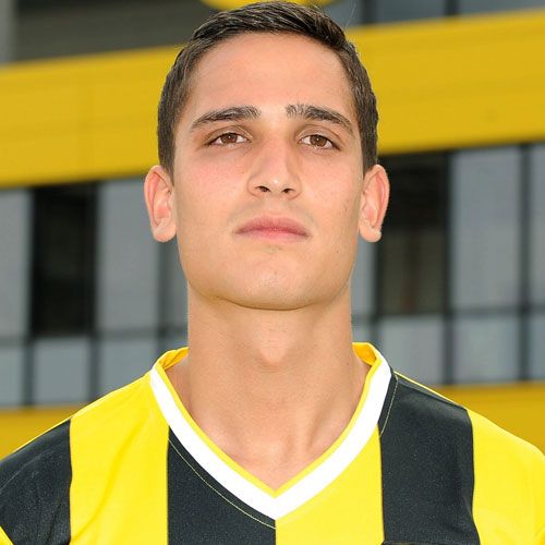 Ein junger Mann mit kurzen, dunklen Haaren trägt ein schwarz-gelb gestreiftes Trikot und steht vor einer gelb-schwarzen Hintergrundwand.