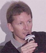 Ein Mann mit kurzer Frisur spricht in ein Mikrofon während einer Veranstaltung.