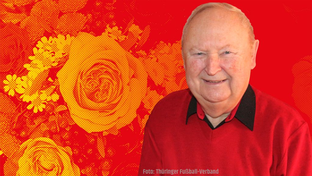 Ein älterer Mann mit lächelndem Gesicht trägt ein rotes Oberteil, vor einem blühenden Blumenmuster in warmen Farben.