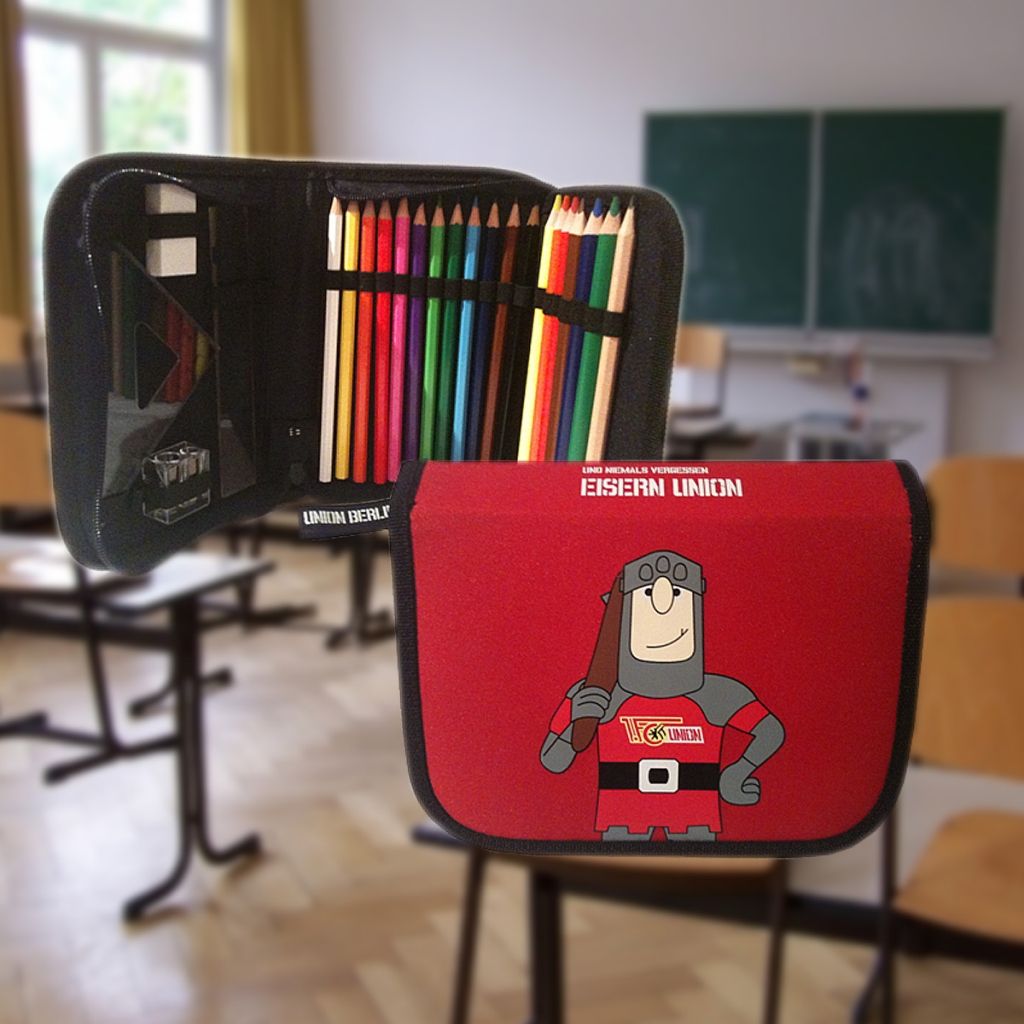 Bunt bemaltes Federmäppchen mit verschiedenen Stiften und einem Comic-Charakter vorne, auf einem Schreibtisch in einem Klassenzimmer.