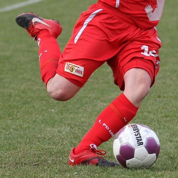 Ein Spieler in roter Sportkleidung tritt einen Fußball auf einem grünen Spielfeld.