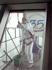 Eine Person in Schutzkleidung steht auf einer hohen Plattform und putzt ein Fenster, während die Sicht begrenzt ist.