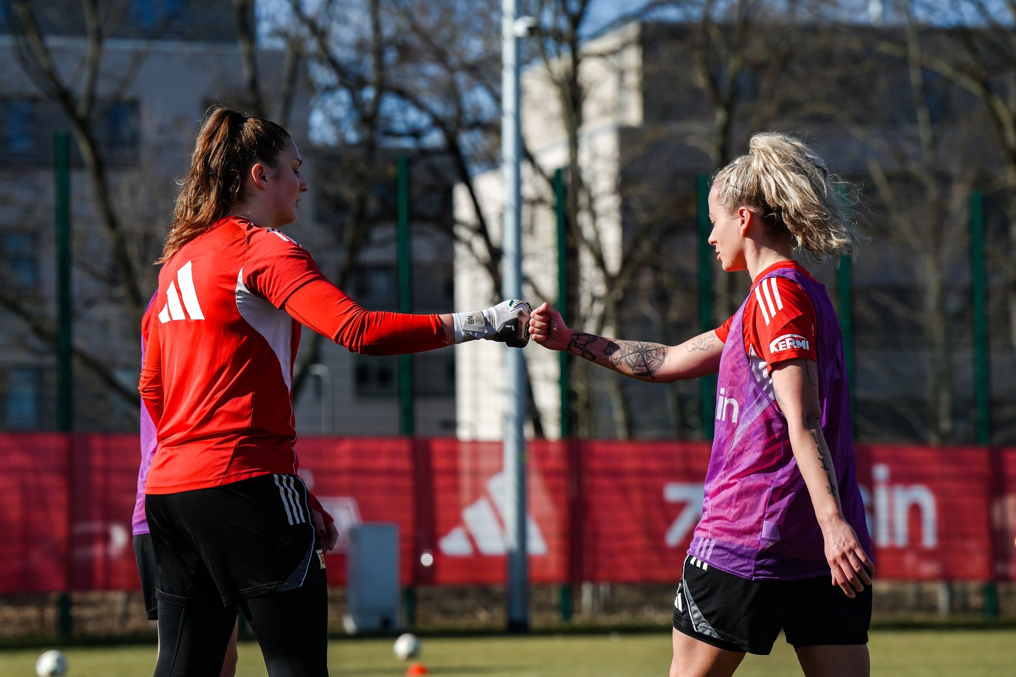 Zwei Fußballspielerinnen, eine in Torwarttrikots, geben sich ein "Fist Bump" während des Trainings auf dem Spielfeld.