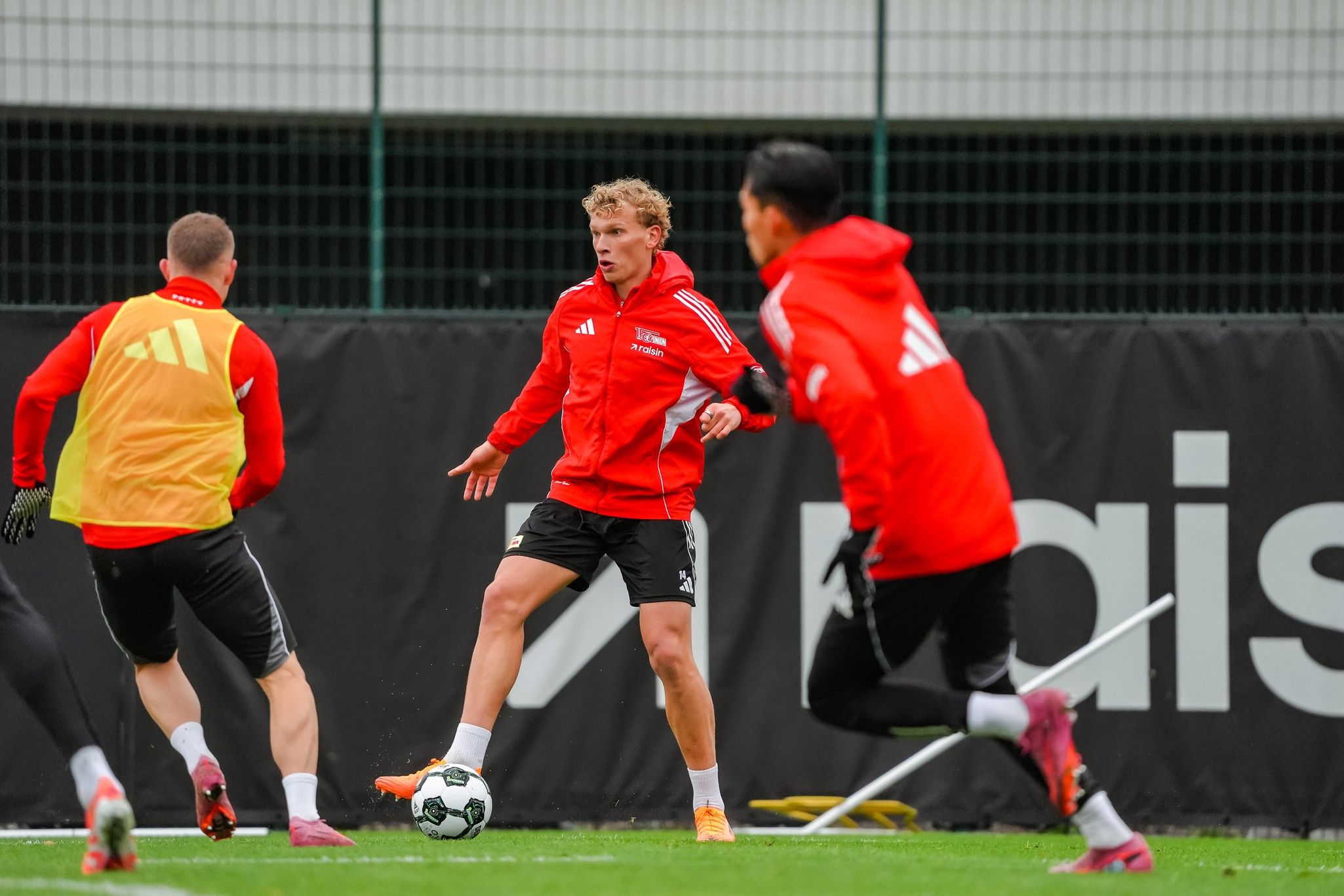 Fußballspieler in roten Trainingsanzügen üben auf dem Platz, während ein Spieler den Ball kontrolliert.