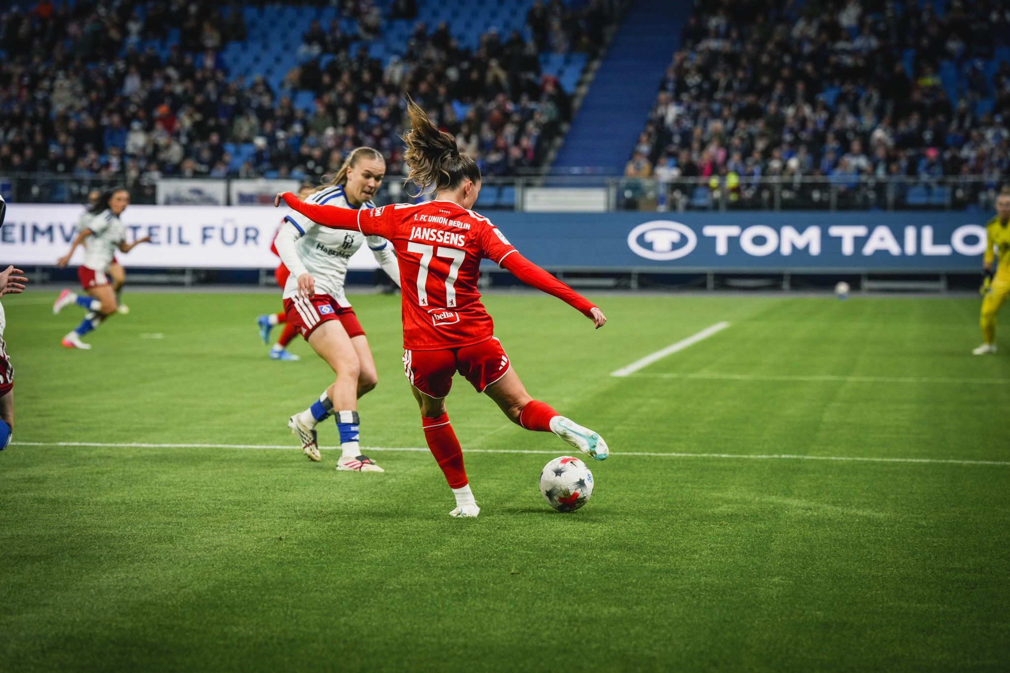 Eine Fußballspielerin mit der Nummer 17 schießt den Ball während eines Spiels auf einem Rasenplatz, umgeben von Zuschauern.