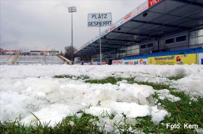Schnee und Eis bedecken den Rasen eines Sportplatzes, auf dem ein Schild mit der Aufschrift "PLATZ GESPERRT" steht.
