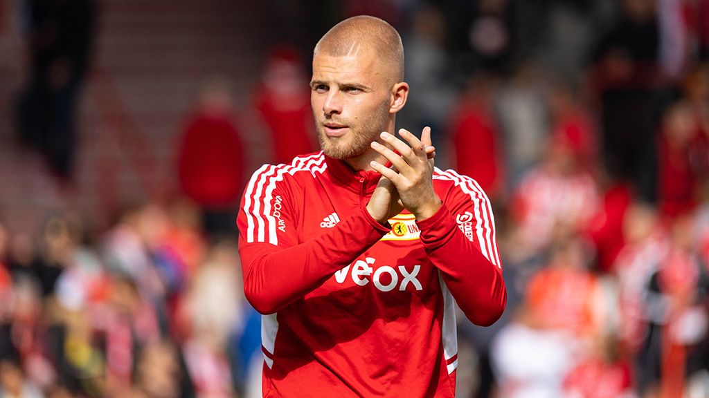 Ein junger Fußballspieler in einem roten Trikot applaudiert vor einer Menschenmenge im Stadion.