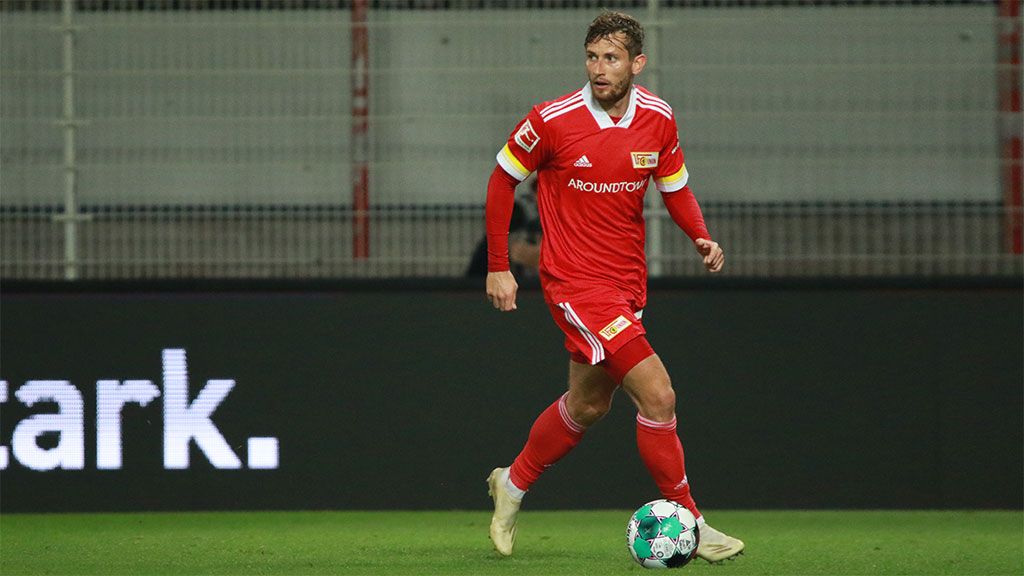 Spieler in rotem Trikot mit Kapitänsbinde dribbelt den Ball auf dem Spielfeld während eines Fußballspiels.