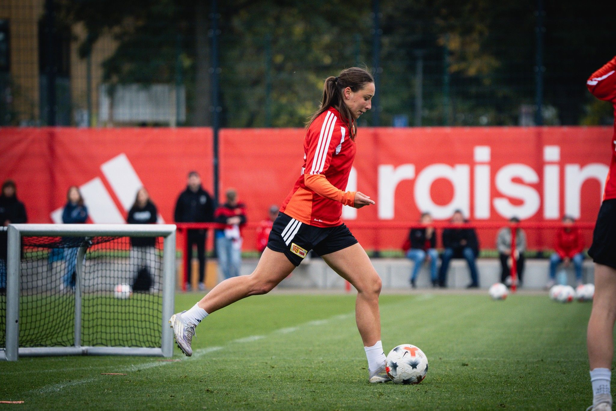 Eine Fußballspielerin in roter Trainingskleidung läuft über den Platz und dribbelt den Ball während des Trainings.