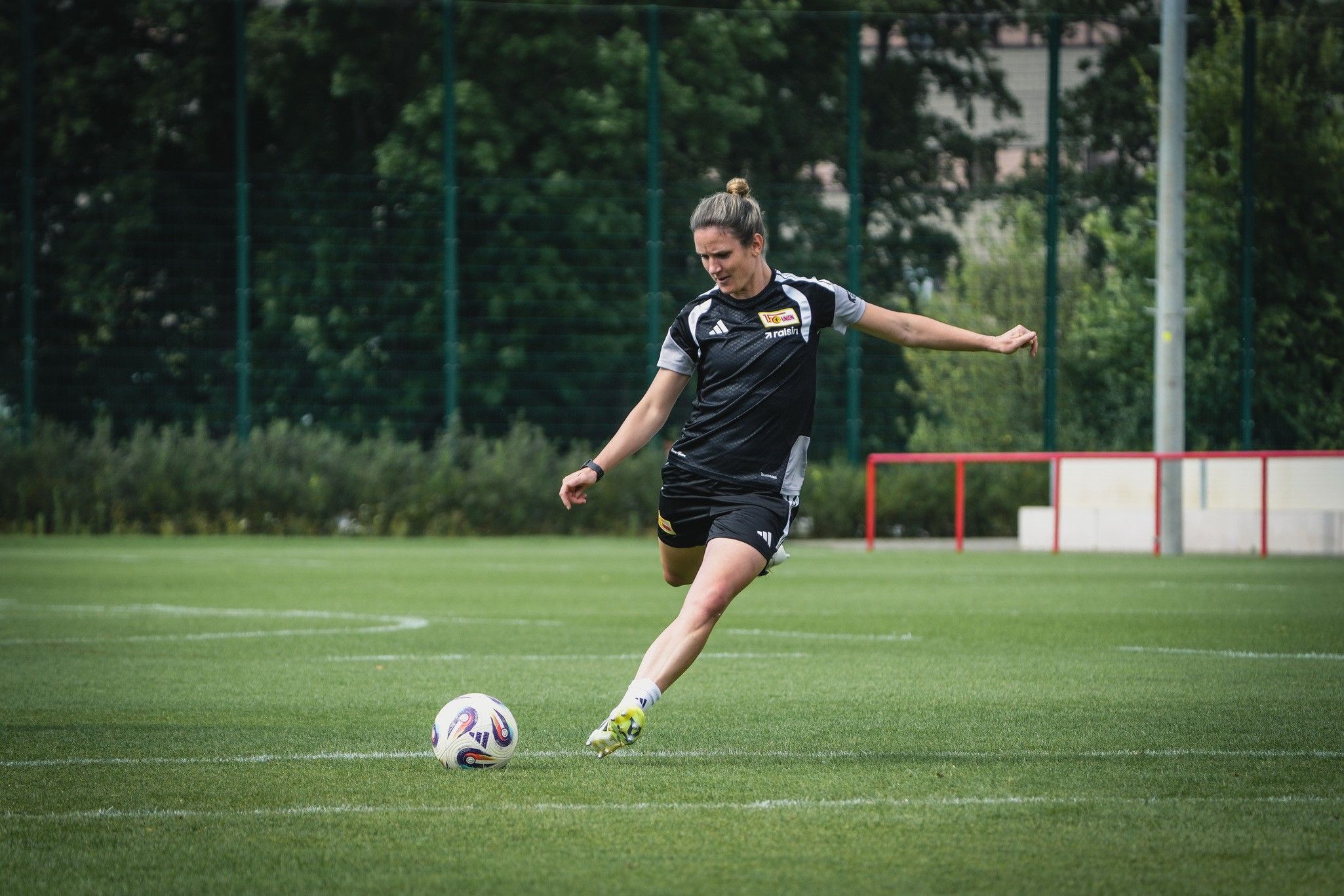 Eine Spielerin in schwarzer Sportkleidung tritt einen Fußball auf einem grünen Trainingsfeld.