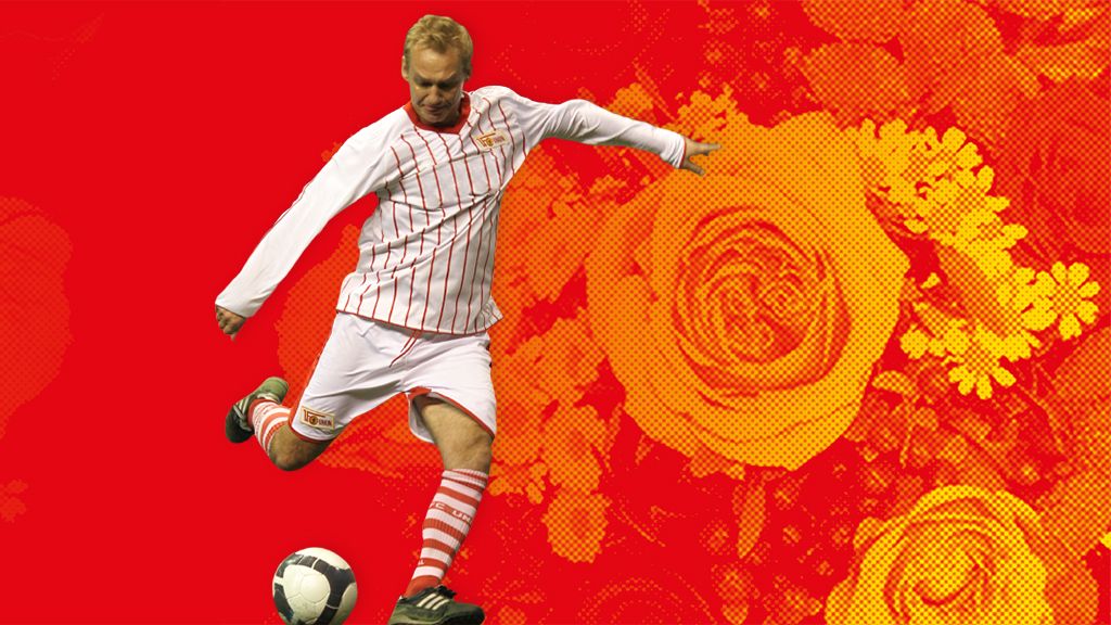 Ein Fußballspieler in einem gestreiften Trikot schießt einen Ball vor einem leuchtend roten Hintergrund mit Blumenmuster.