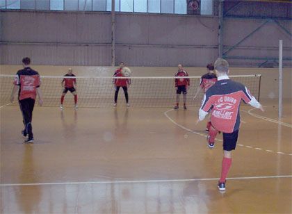 Eine Gruppe von fünf Fußballspielern trainiert in einer Halle, während ein Spieler einen Pass spielt.