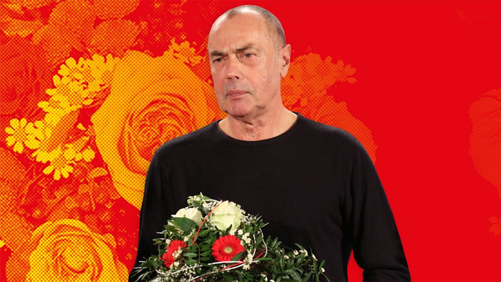Mann in schwarzem Shirt hält einen Blumenstrauß vor einem roten Hintergrund mit floralen Mustern.
