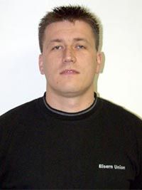 Ein Mann mit kurzen, stacheligen Haaren trägt ein schwarzes Sweatshirt und blickt neutral in die Kamera.