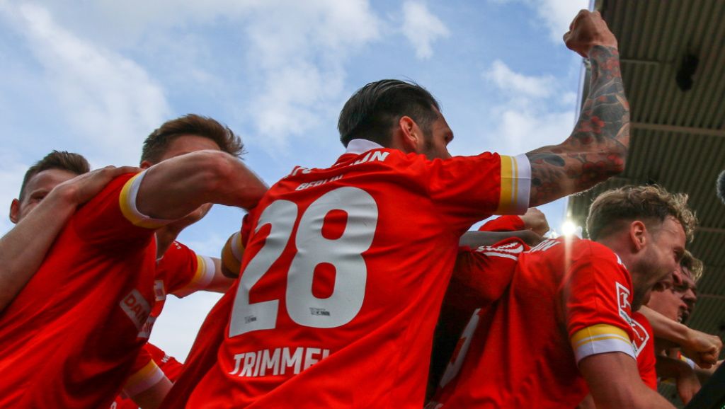 Eine Gruppe von Fußballspielern in rot-weißen Trikots feiert einen Torerfolg auf dem Spielfeld.