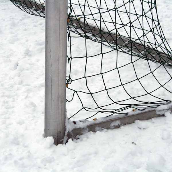 Ein Fußballtor mit einem Netz, das teilweise im Schnee steht. Der Boden ist mit einer Schicht frischem Schnee bedeckt.