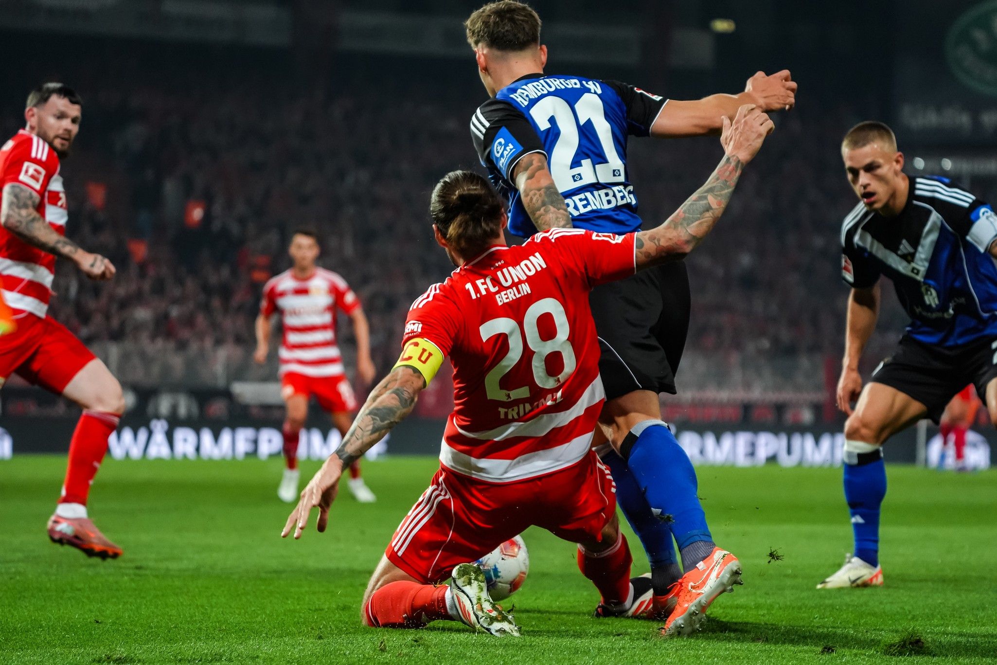 Ein Fußballspiel mit Spielern in roten und blauen Trikots, ein Spieler im roten Trikot fällt zu Boden.