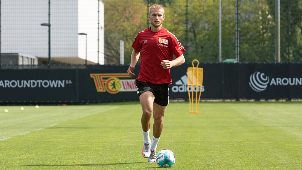 A soccer player runs with a ball on a training field, surrounded by practice markers and goals.