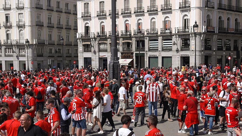 Crowd in red clothing in a square, surrounded by historic buildings, festive atmosphere.