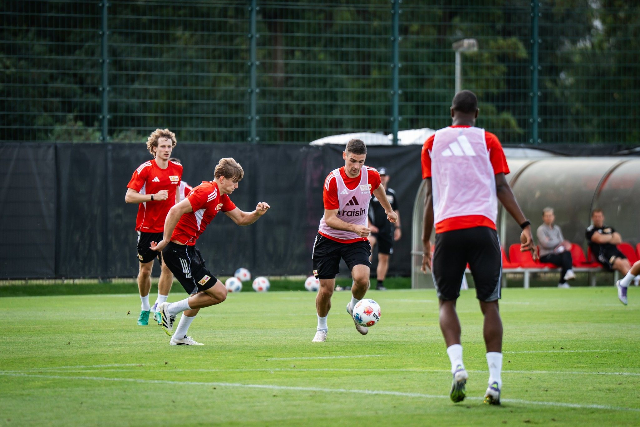 Gruppe von Fußballspielern in roten Trikots trainiert auf einem Rasenplatz mit einem Ball.