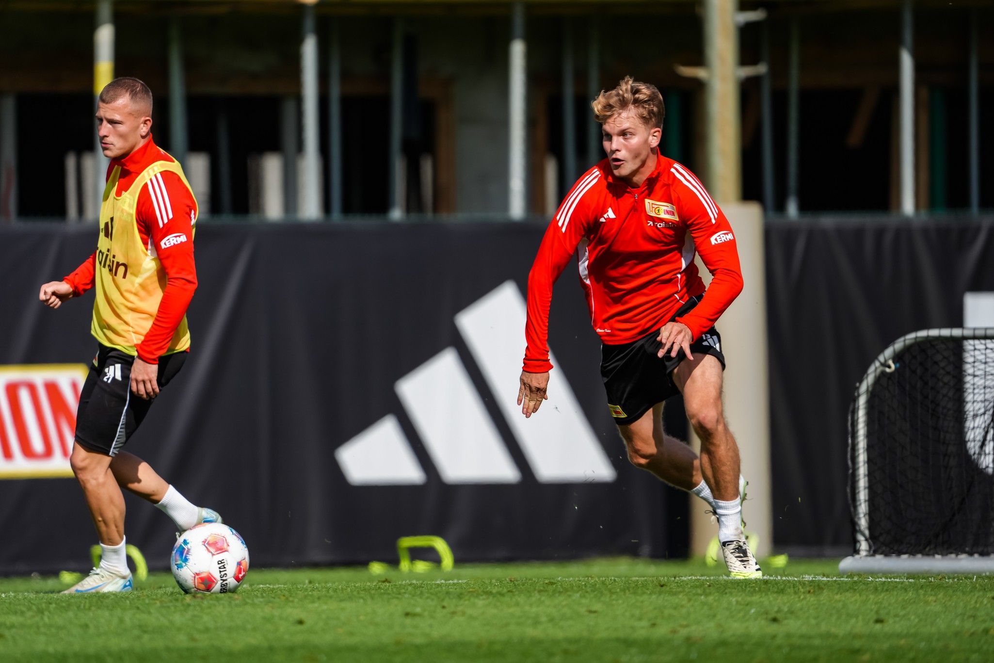 Zwei Fußballspieler trainieren auf einem Platz, einer sprintet, der andere steht in der Nähe und beobachtet.