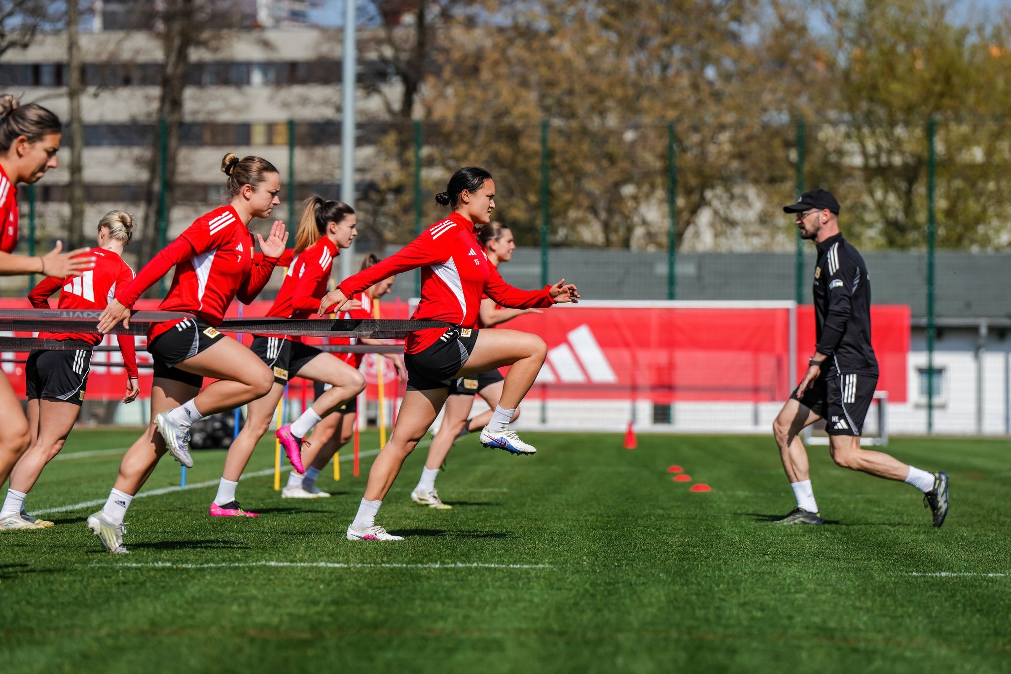 Frauenfußballmannschaft beim Training auf einem Rasenplatz, während sie mit einem Widerstandsband sprinten.