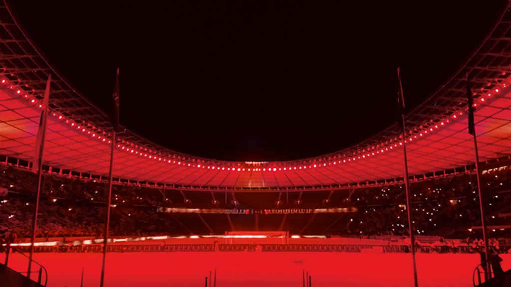 Ein Stadion mit rotem Licht, leeren Zuschauerplätzen und einer hohen, geschwungenen Kuppelstruktur.