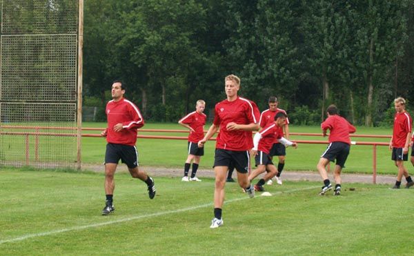 Eine Gruppe von Fußballspielern in roten Trikots trainiert auf einem grünen Sportplatz.