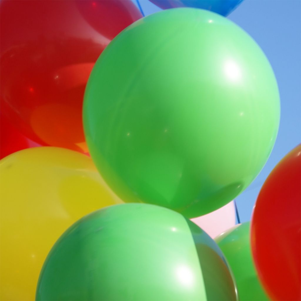Bunte, glänzende Luftballons in Rot, Gelb, Grün und Blau vor einem blauen Himmel.