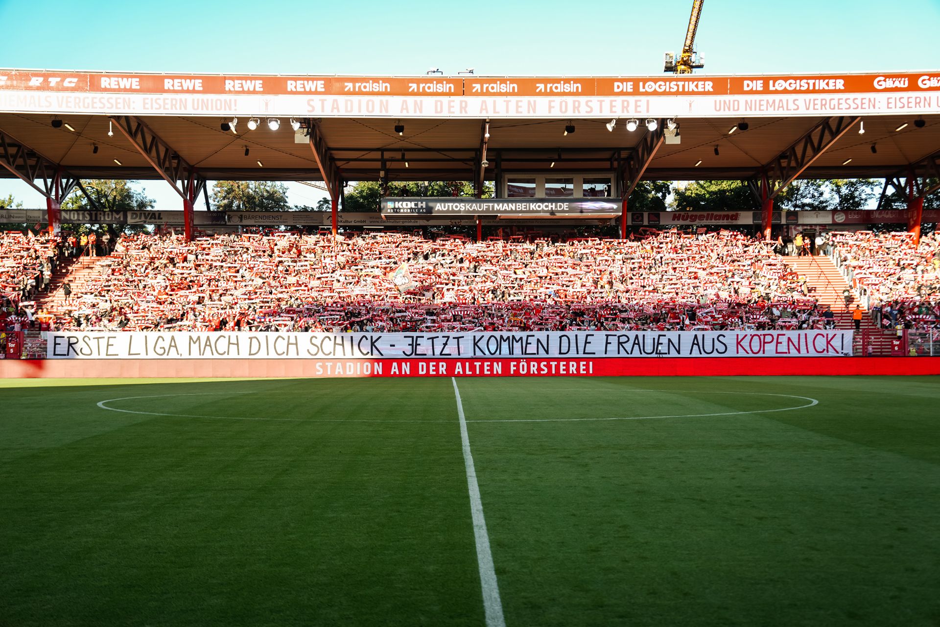 Stadion mit Zuschauern; Banner im Vordergrund: "ERSTE LIGA MACH DICH SCHICK - JETZT KOMMEN DIE FRAUEN AUS KOPENICK!"