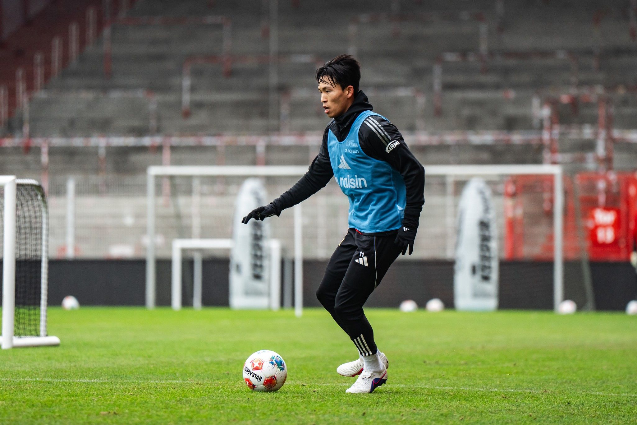 Ein Fußballspieler in Trainingskleidung übt auf einem Rasenplatz mit Toren im Hintergrund.