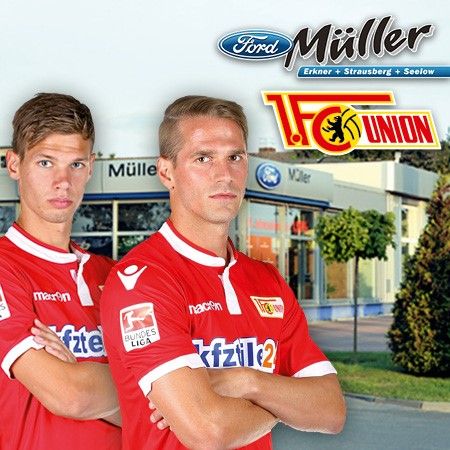Zwei Fußballspieler des 1. FC Union Berlin in roten Trikots vor einem Autohaus mit dem Logo "Ford Müller".