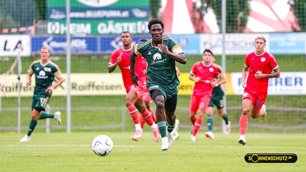 Ein Fußballspieler in grüner Uniform sprintet auf dem Spielfeld, während andere Spieler ihm näher kommen.