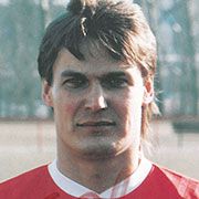 Porträt eines männlichen Fußballspielers in einem roten Trikot, mit mittellangen, dunklen Haaren und neutralem Gesichtsausdruck.