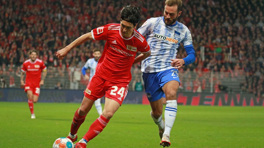 Two soccer players in action, one in a red jersey with the number 24 and the other in a striped jersey.