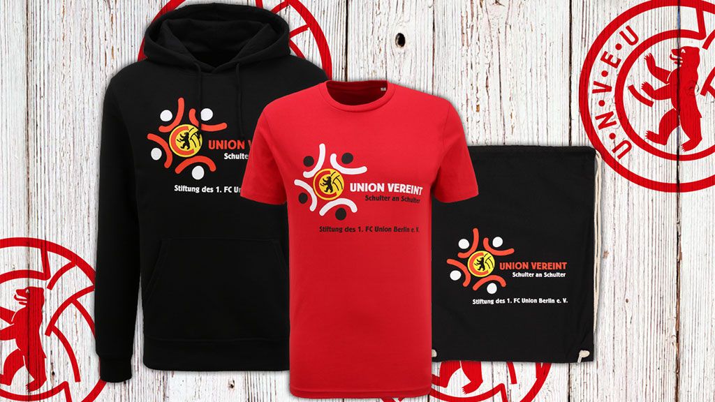 Drei Kleidungsstücke in Schwarz und Rot mit dem Logo von Union Verein auf einem Holz-Hintergrund.