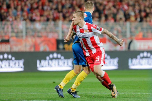 Two football players in the game, one in red and white, the other in blue jerseys, in the stadium during a competition.