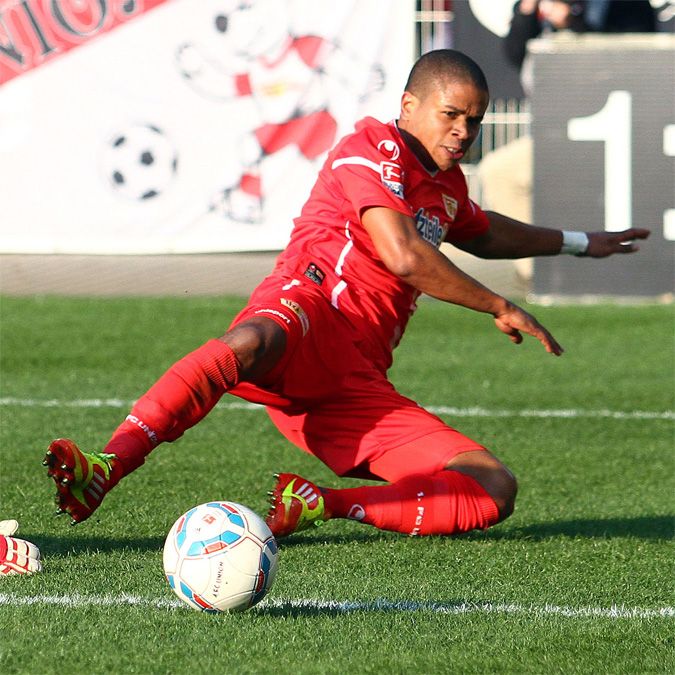 Ein Fußballspieler in roter Ausrüstung rutscht auf dem Rasen, um den Ball zu erreichen.