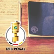 DFB-Pokal-Trophäe neben einem Stift und einem Notizbuch auf einer Holzoberfläche.