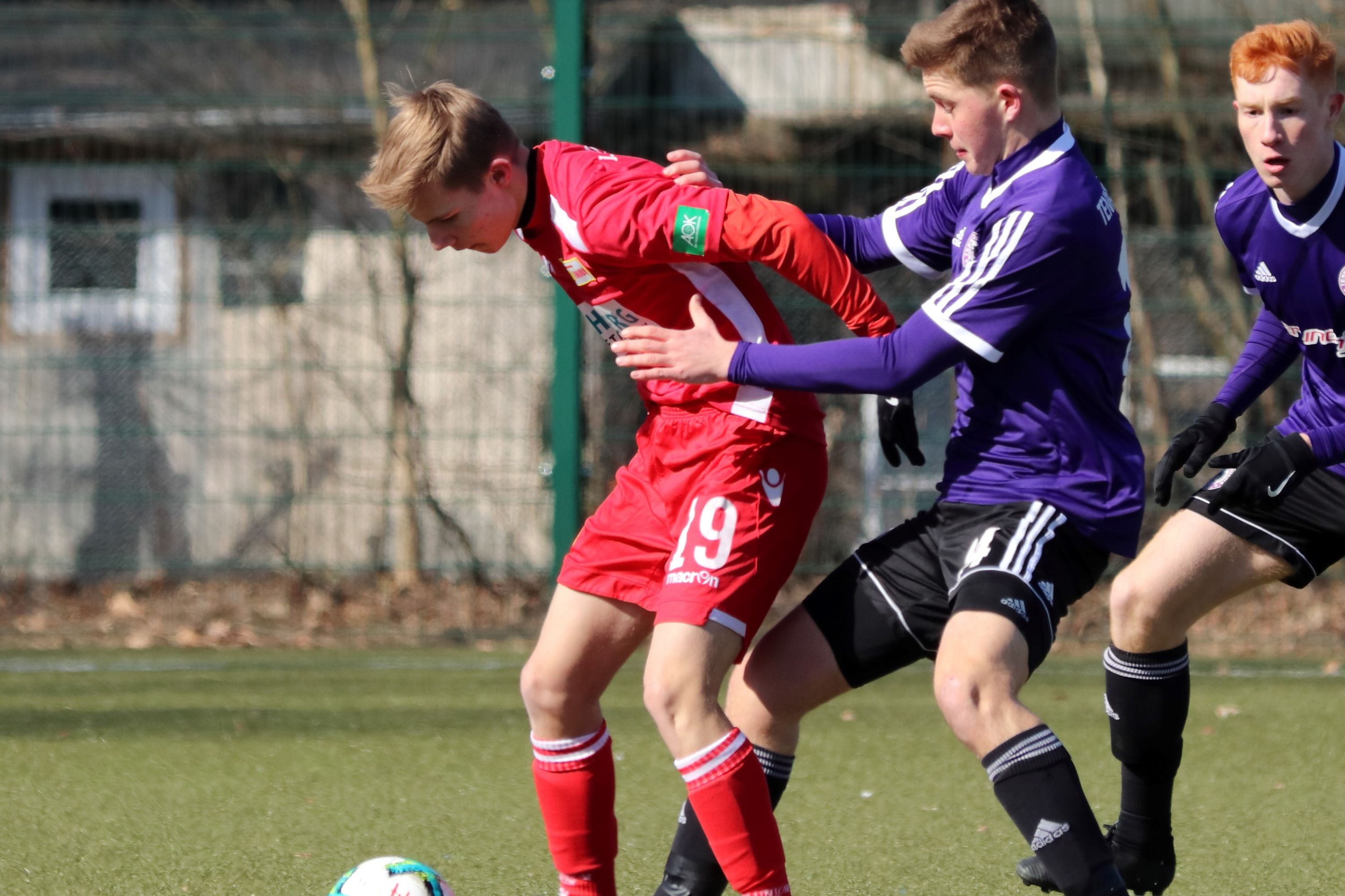 Zwei junge Fußballspieler im Wettkampf um den Ball auf einem Kunstrasenplatz.