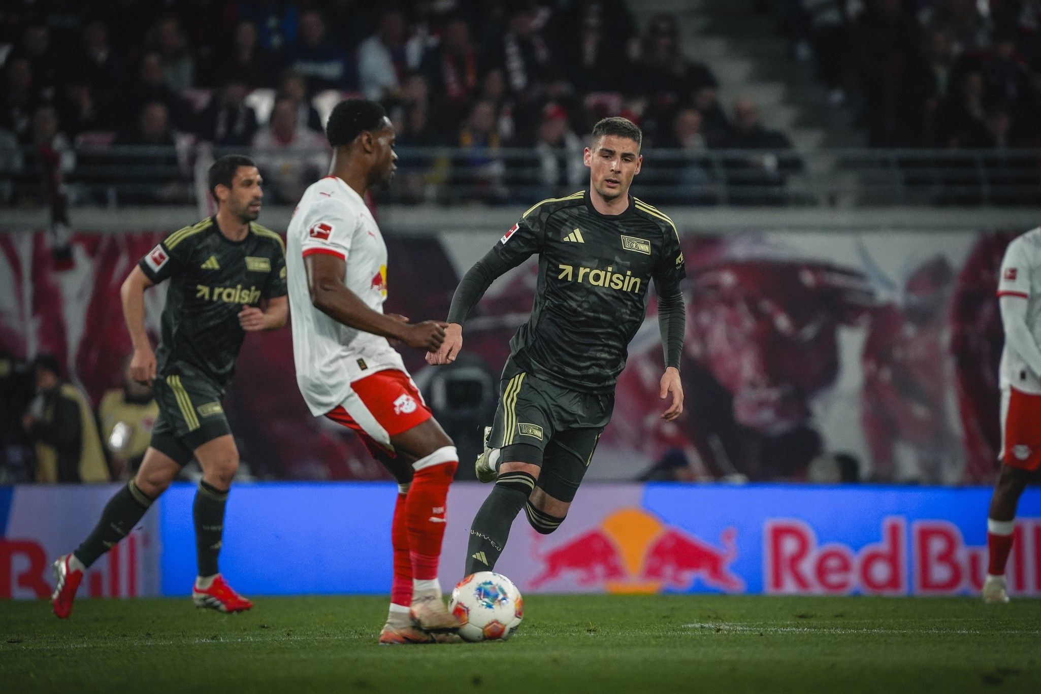 Fußballspiel: Zwei Spieler in actionreichem Moment, ein Spieler dribbelt, während ein anderer verteidigt. Zuschauer im Hintergrund.