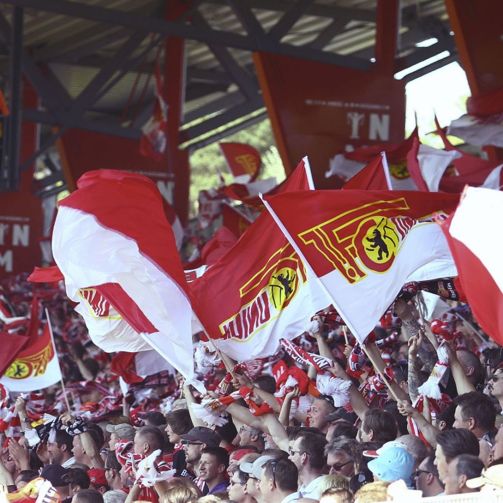 Menschenmenge in einem Stadion, die mit roten und weißen Fahnen und Schals ihre Unterstützung zu einem Team zeigt.